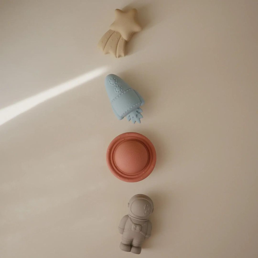 De vier mushie ruimte badspeeltjes, bestaande uit een komeet, raket, planeet en astronaut, liggen op een rij.
