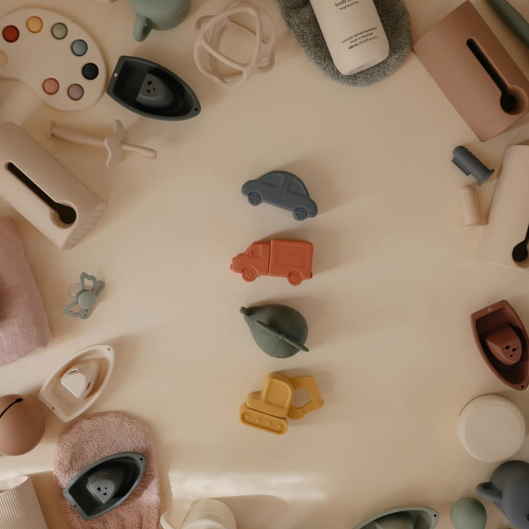 Een bovenaanzicht van diverse mushie badspeeltjes en babyproducten, waaronder de vier voertuigen in het midden.