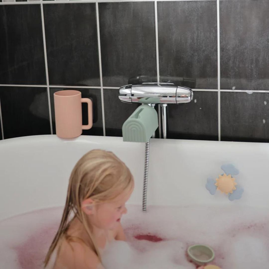 Een kind speelt in bad met bubbels, met de mushie blush badspoelbeker op de rand van het bad.