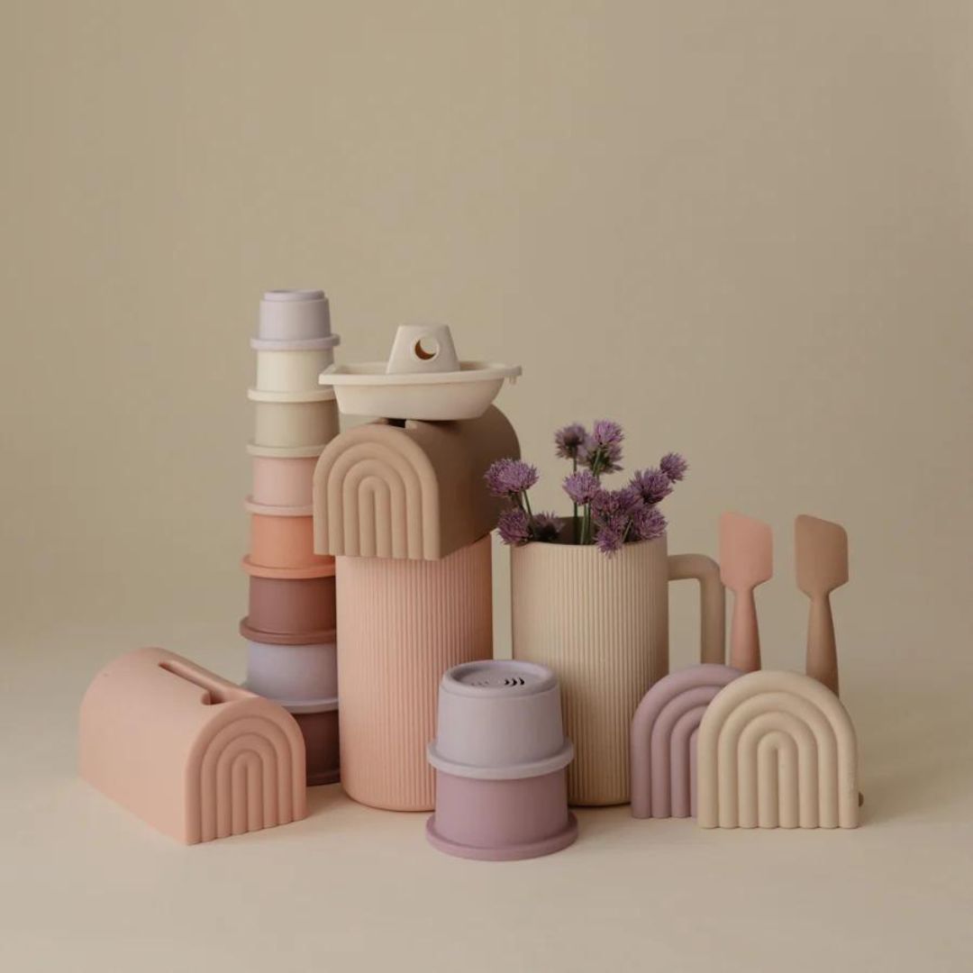 Een collectie mushie babyspeelgoed in pastelkleuren, waaronder stapeltorens en de badspoelbeker.