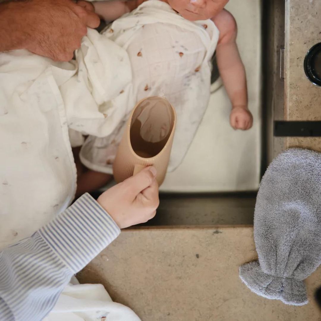 Een volwassene spoelt een baby af met de mushie badspoelbeker tijdens het badderen.