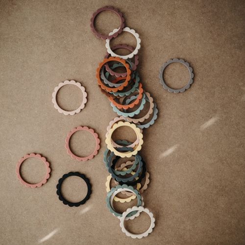 Een collectie mushie bijtring armbanden in verschillende kleuren ligt verspreid op een bruine ondergrond.
