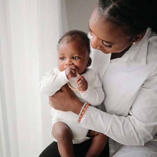 Een baby wordt vastgehouden door een volwassene en bijt op een mushie bijtring armband.
