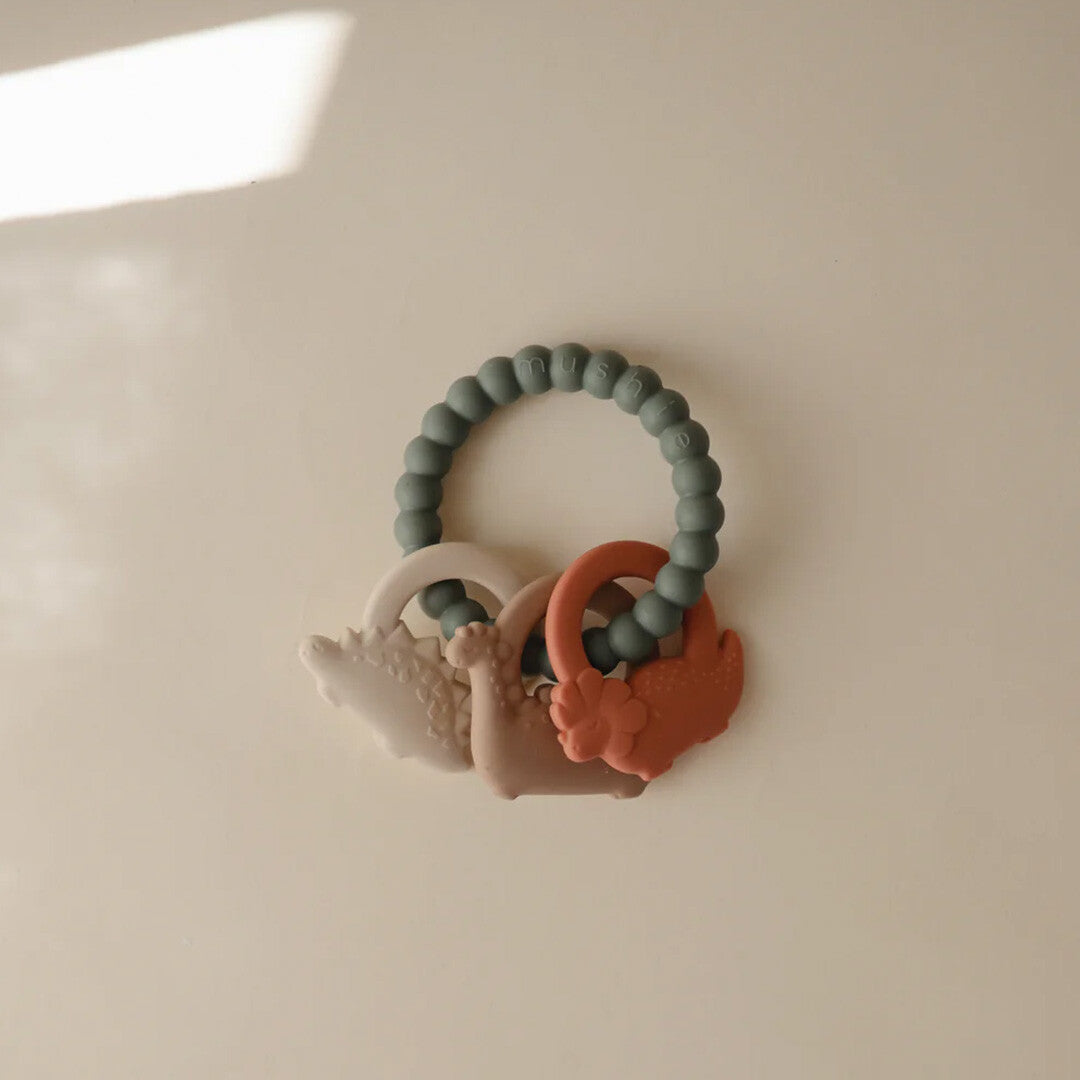 Mushie bijtspeelgoed met een groene ring en drie dinosaurusvormige bijtringen.