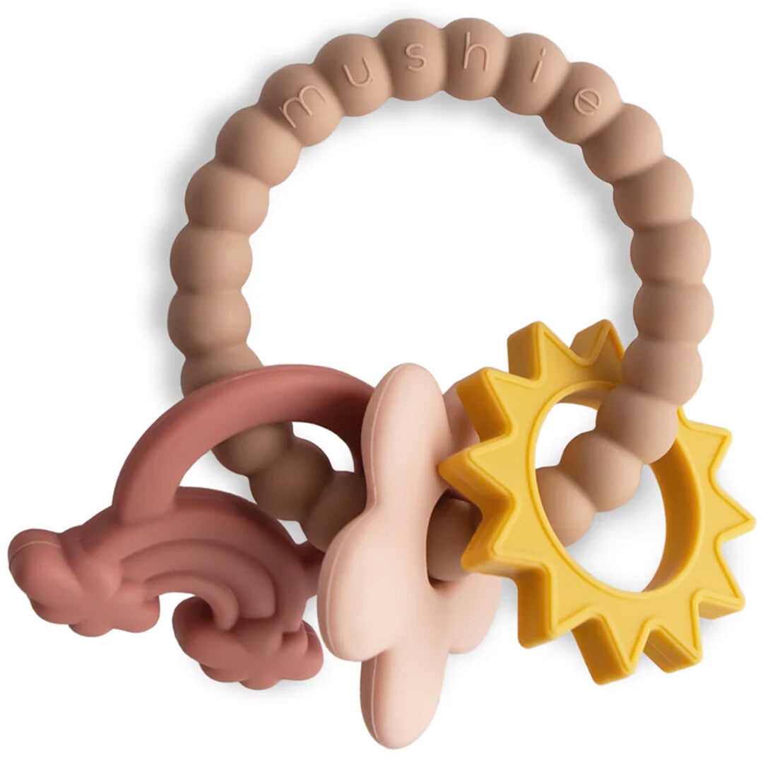 Mushie siliconen bijtring met beige ring en hangers in de vorm van een roze regenboog, lichtroze bloem en gele zon.