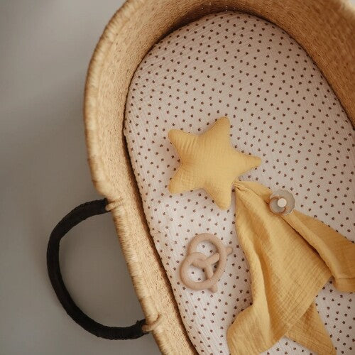 Een beige pretzel bijtring, een gele ster en een gele doek liggen in een wiegje.