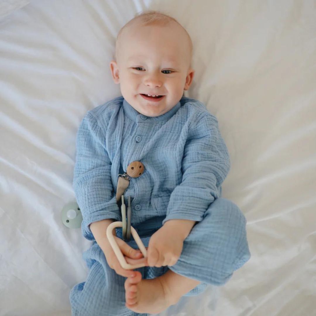 Lachende baby in een blauw pakje die een mushie bijtring sleutelbos vasthoudt.