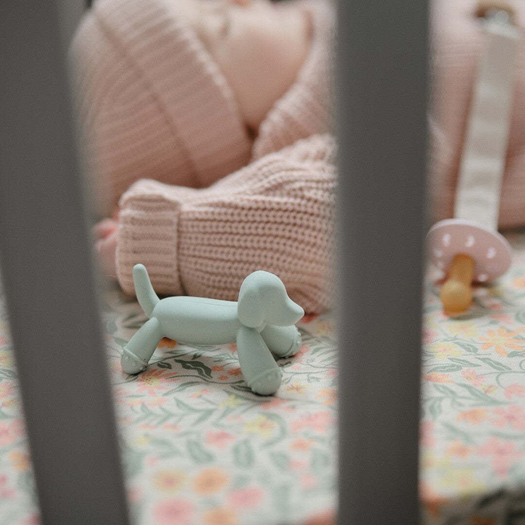 Groene mushie bijtspeelgoed hond in een wieg, met een baby en speen op de achtergrond.