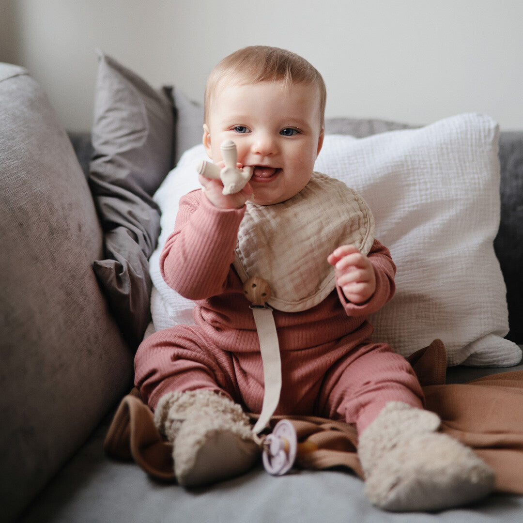 Een lachende baby met het mushie bijtspeelgoed lammetje in de mond.