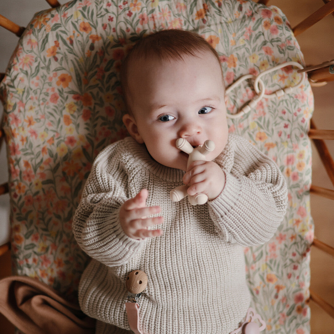 Een baby ligt in een wieg en houdt het mushie bijtspeelgoed lammetje vast.