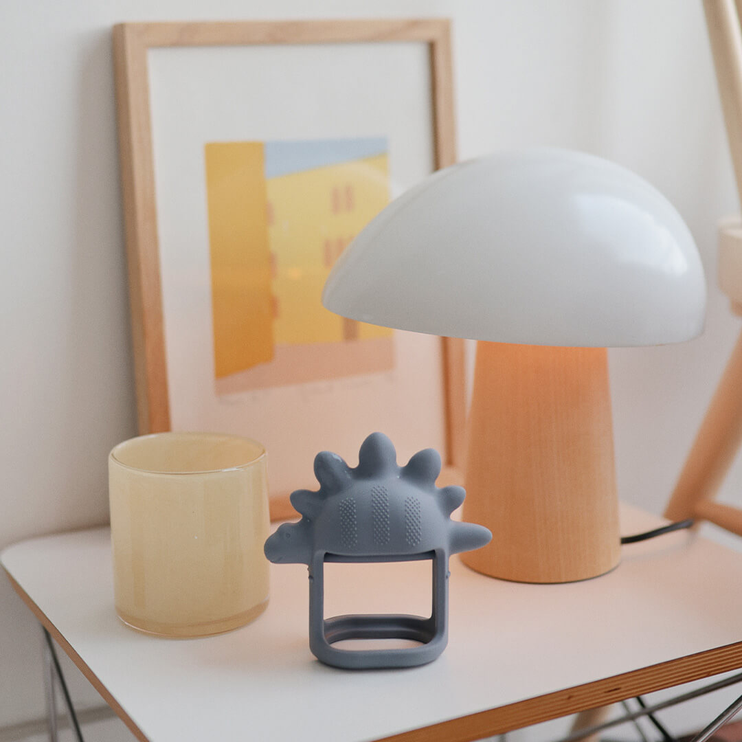 Het grijze dinosaurus bijtspeelgoed staat op een nachtkastje naast een lamp en een glas.