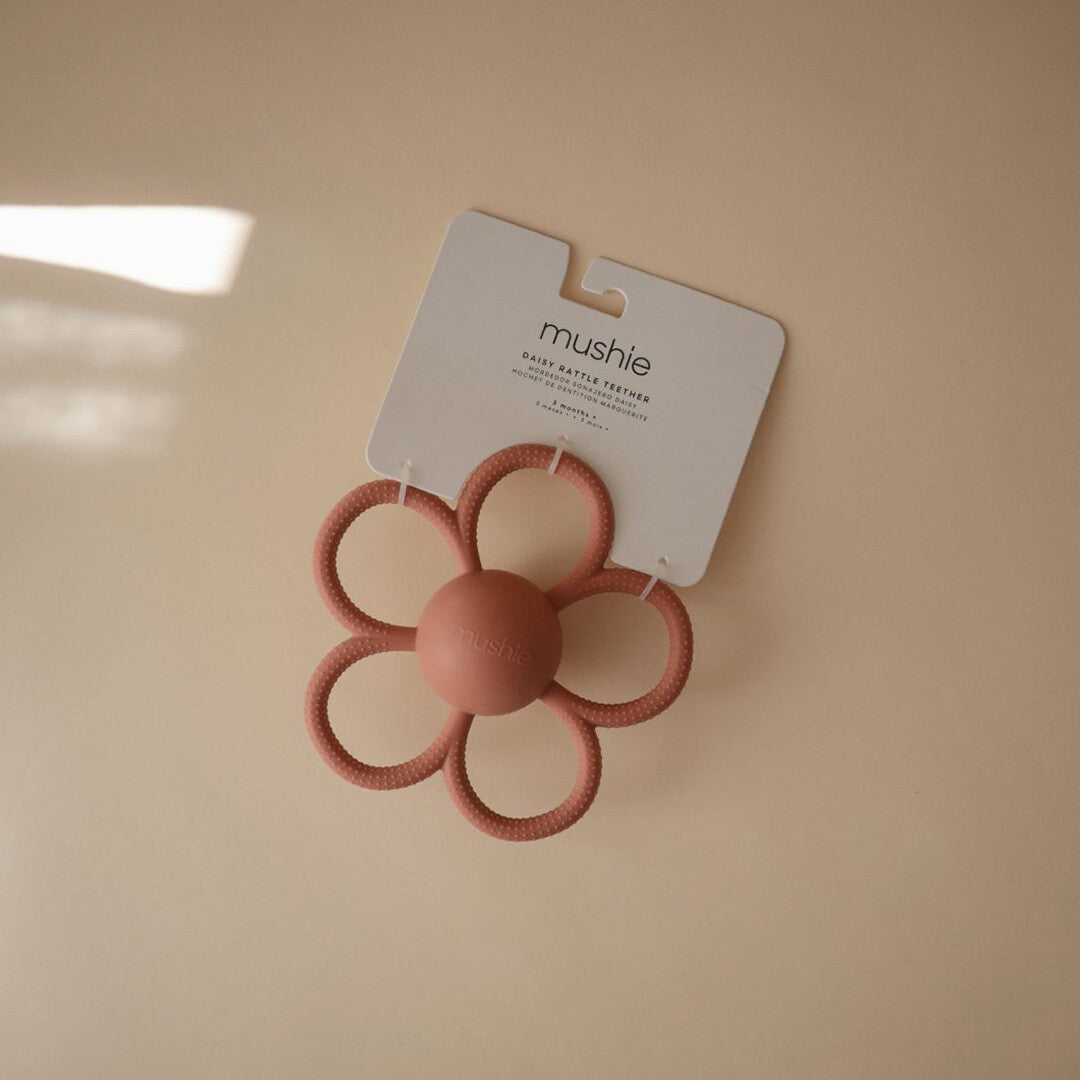 Het roze mushie bijtspeelgoed in de vorm van een bloem op de verpakking.