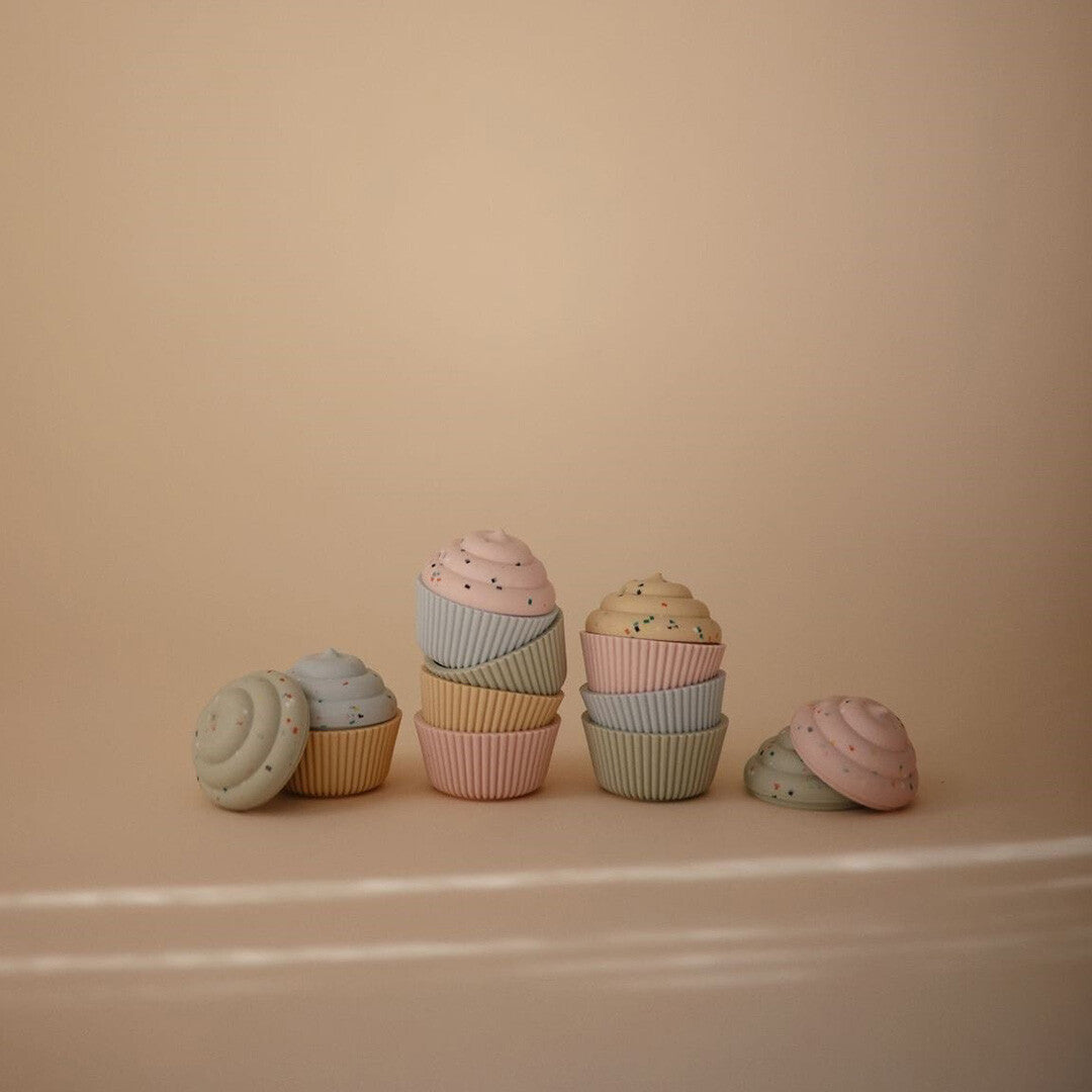 Een collectie mushie siliconen speelgoedcupcakes in pastelkleuren, deels gestapeld, op een lichte ondergrond.