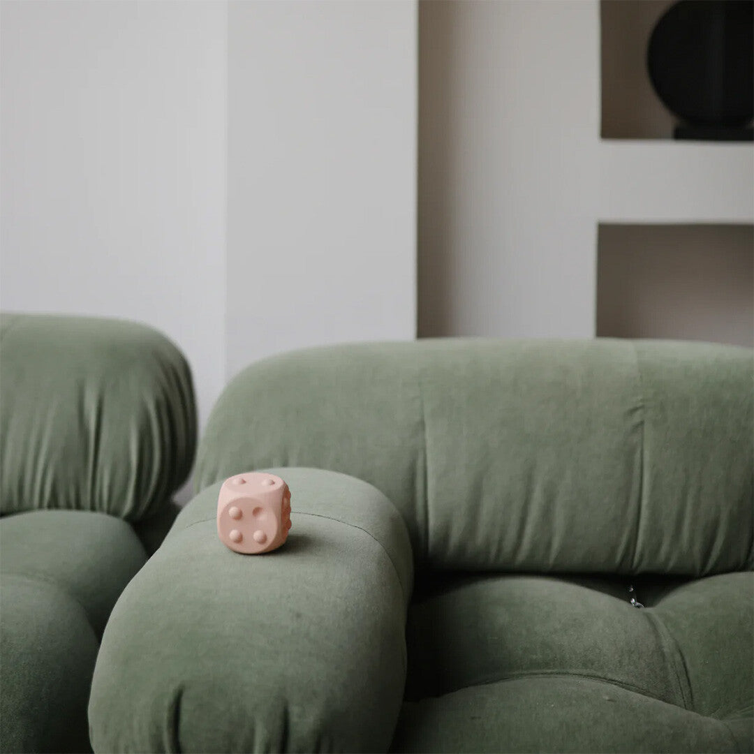 Een blush roze mushie siliconen sensorische dobbelsteen ligt op de armleuning van een groene bank.