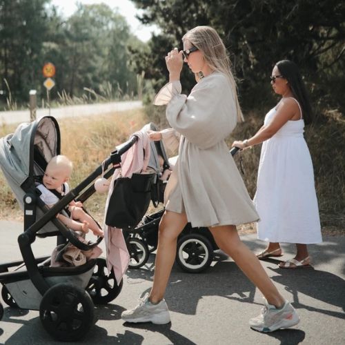 Twee vrouwen wandelen met baby's in kinderwagens buiten.