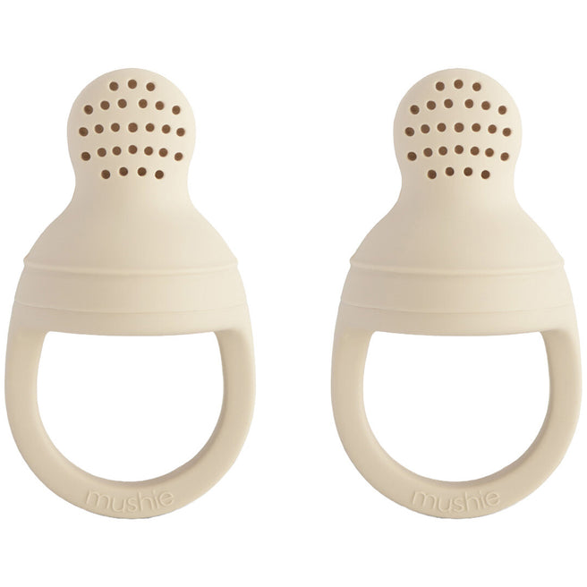 Twee beige Mushie siliconen fruitspenen met geperforeerde bovenkant en handvat.