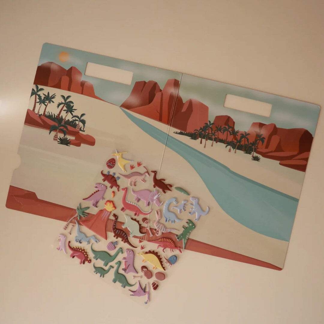 De Mushie herbruikbare dinosaurusstickers liggen op de opengeklapte landschapsachtergrond.