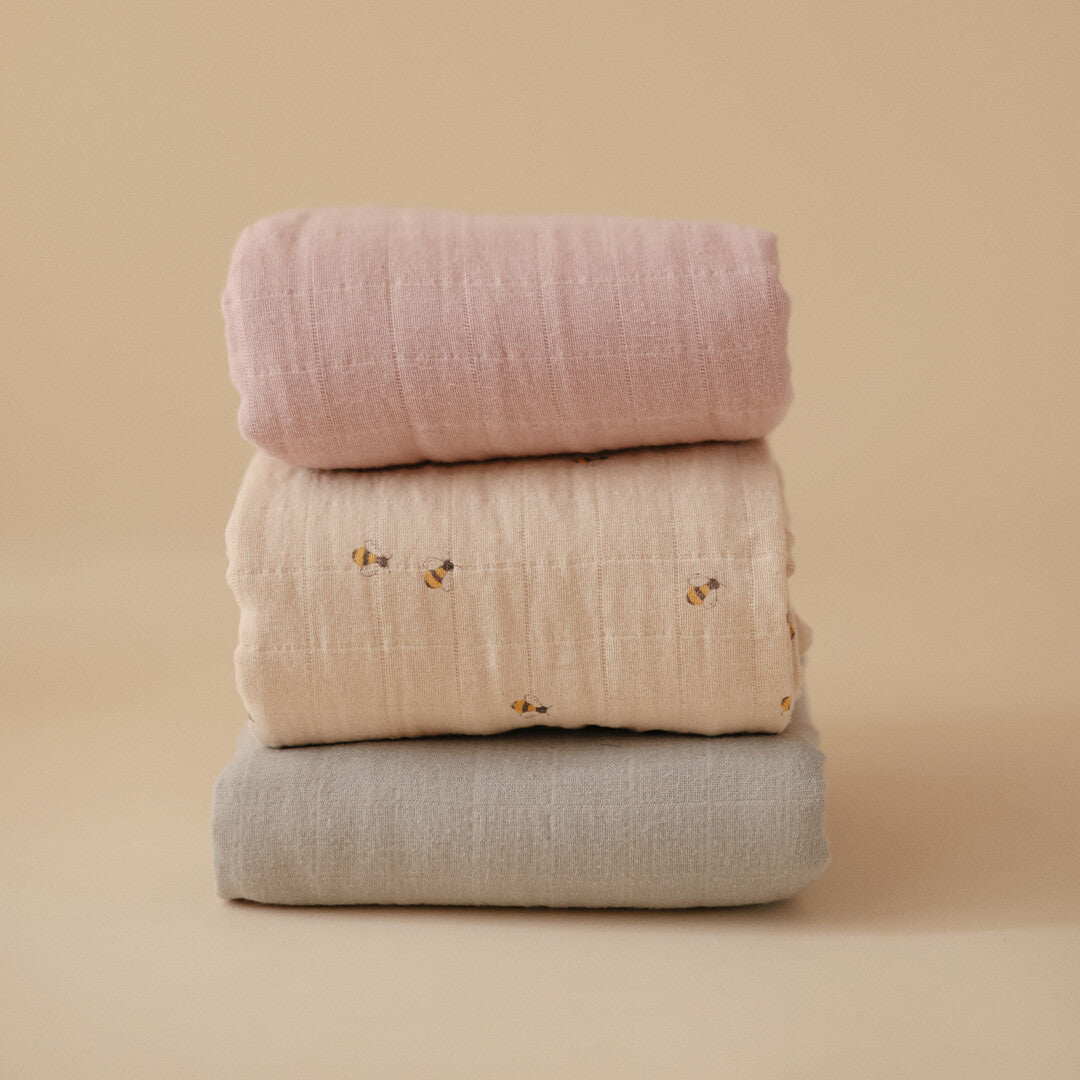 Drie opgerolde mushie inbakerdoeken in roze, beige met bijen en grijs.