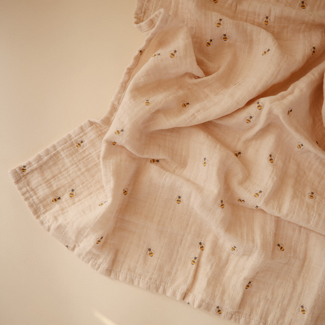 Detail van de beige mushie inbakerdoek met bijenpatroon.