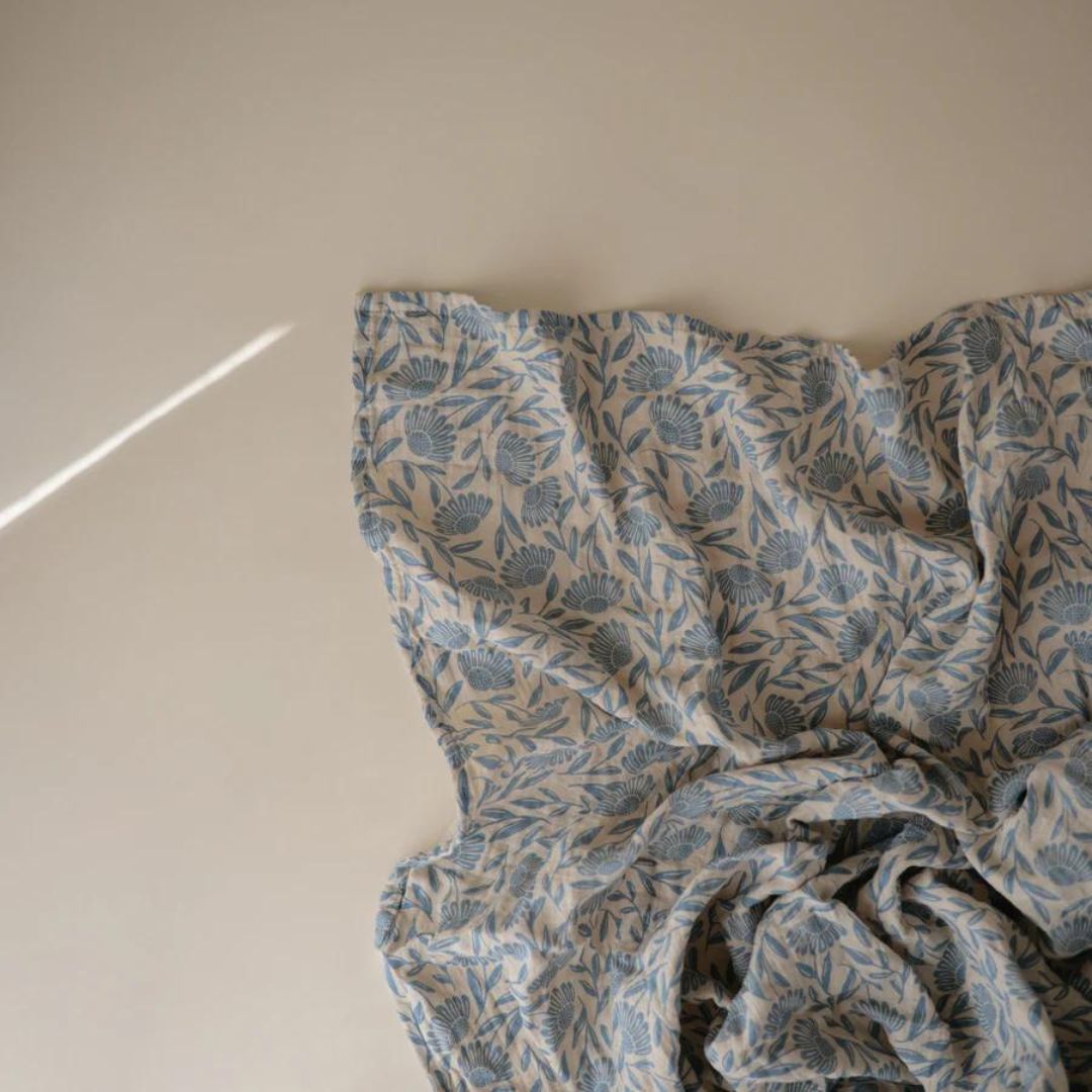 Losjes gedrapeerde mushie inbakerdoek met blauw bloemenpatroon op een lichte ondergrond.