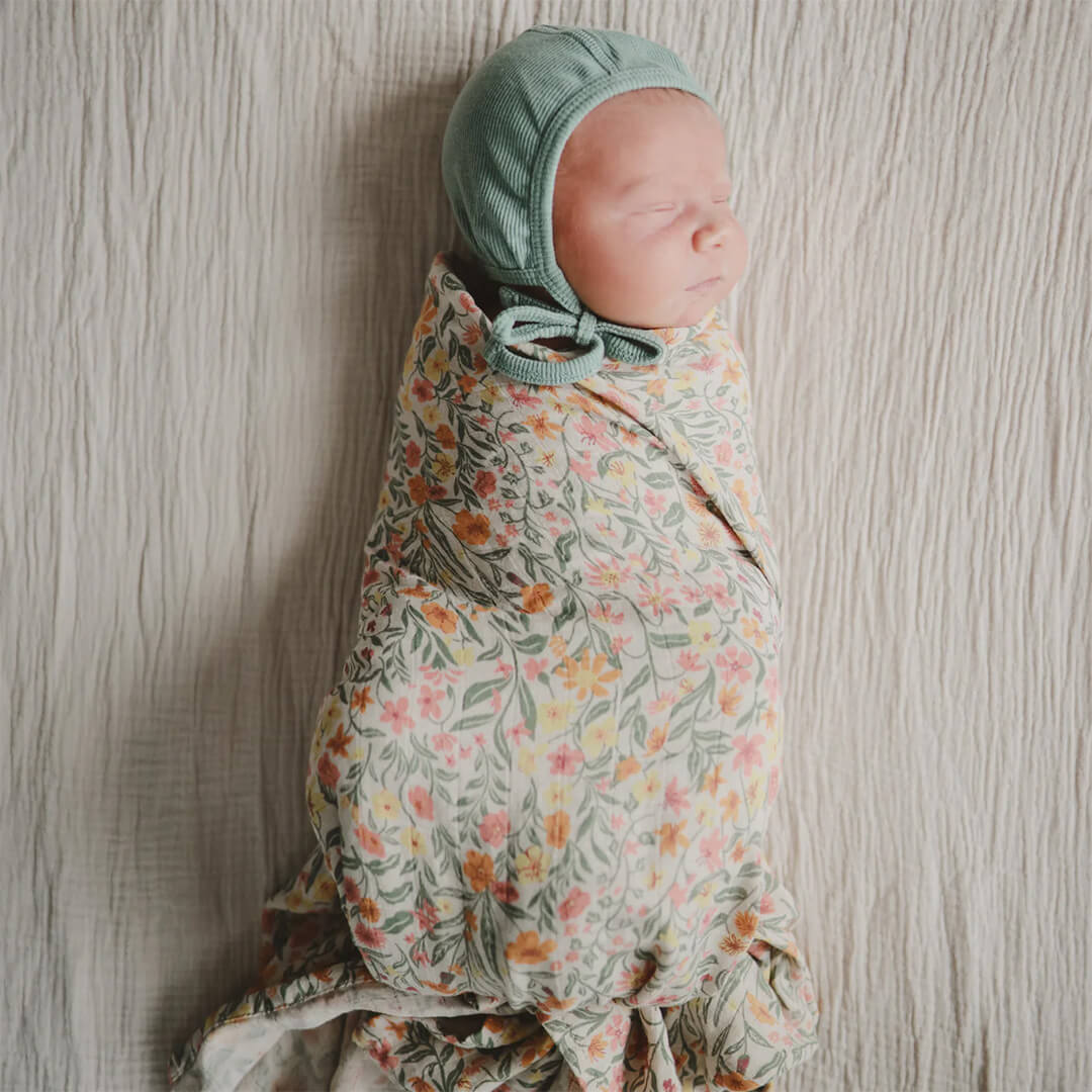 Slapende baby ingebakerd in de Mushie inbakerdoek met pastel bloemenpatroon.