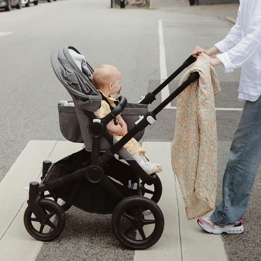 Mushie inbakerdoek met pastel bloemenpatroon hangt over een kinderwagen met baby.