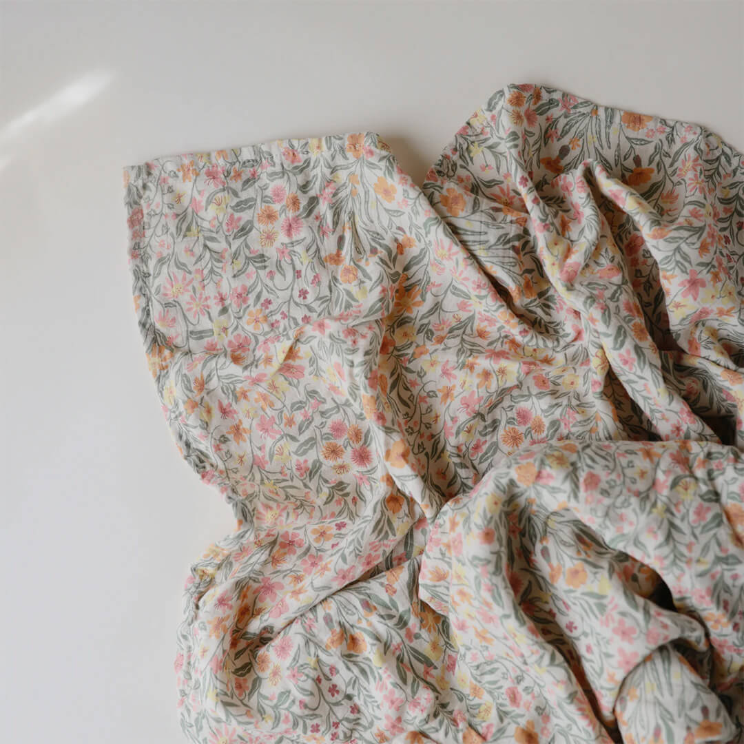 Detail van de Mushie inbakerdoek met pastel bloemenpatroon op een witte ondergrond.