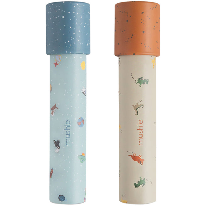 Twee Mushie kaleidoscopen, een blauwe met ruimte-thema en een beige met dinosaurus-thema, staan rechtop.