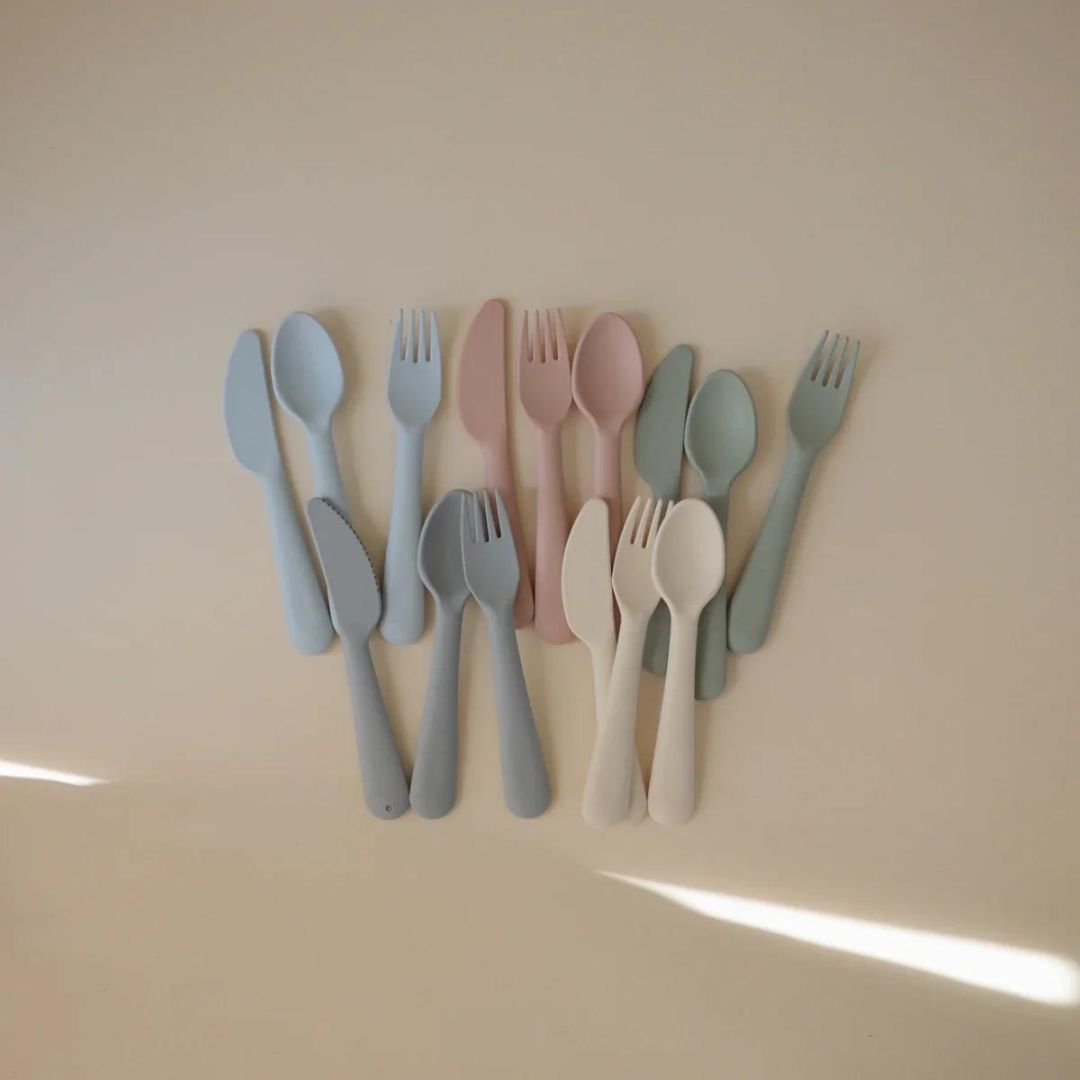 Collectie mushie kinderbestek in verschillende pastelkleuren op een lichte ondergrond.
