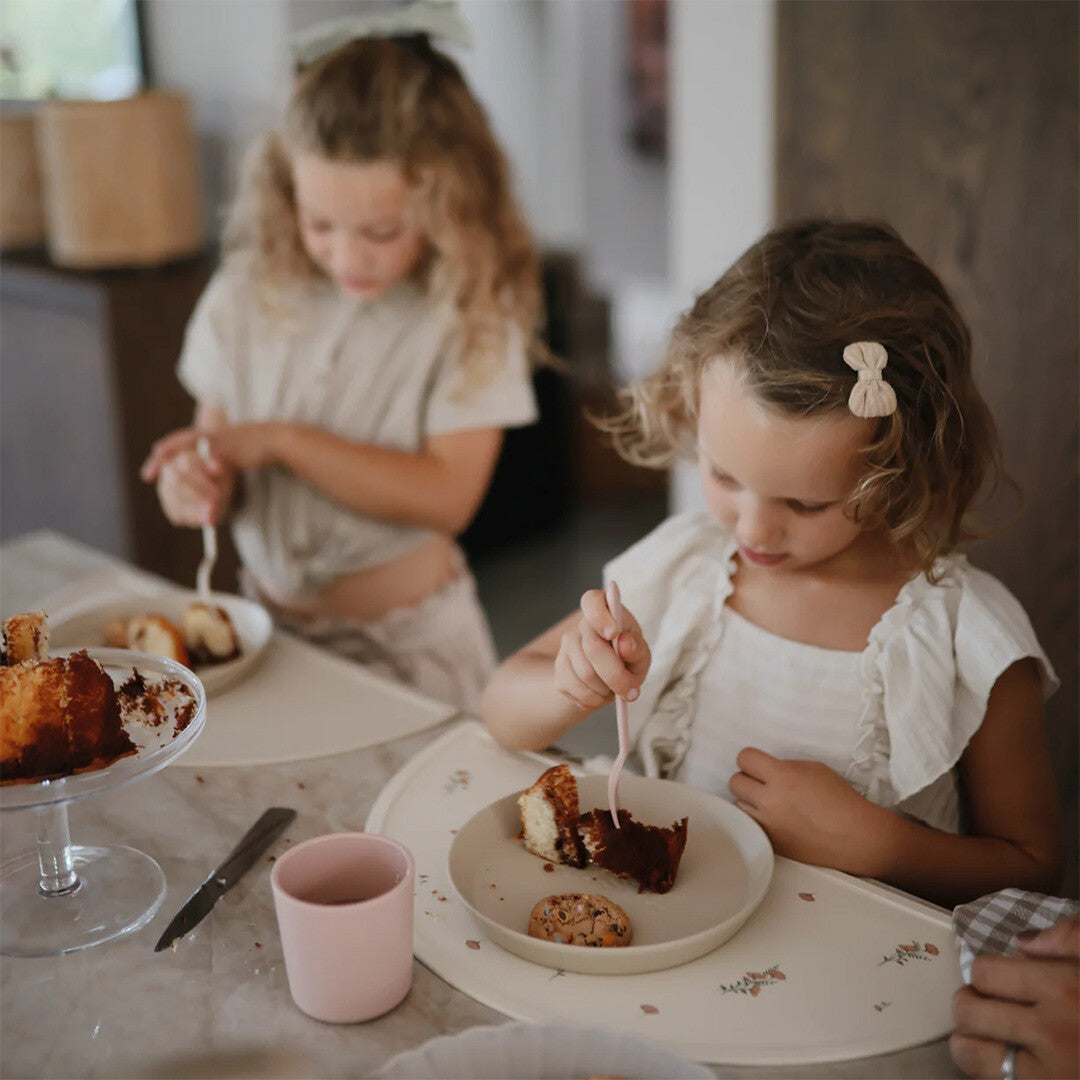 Twee meisjes eten cake van beige kinderborden aan een tafel.
