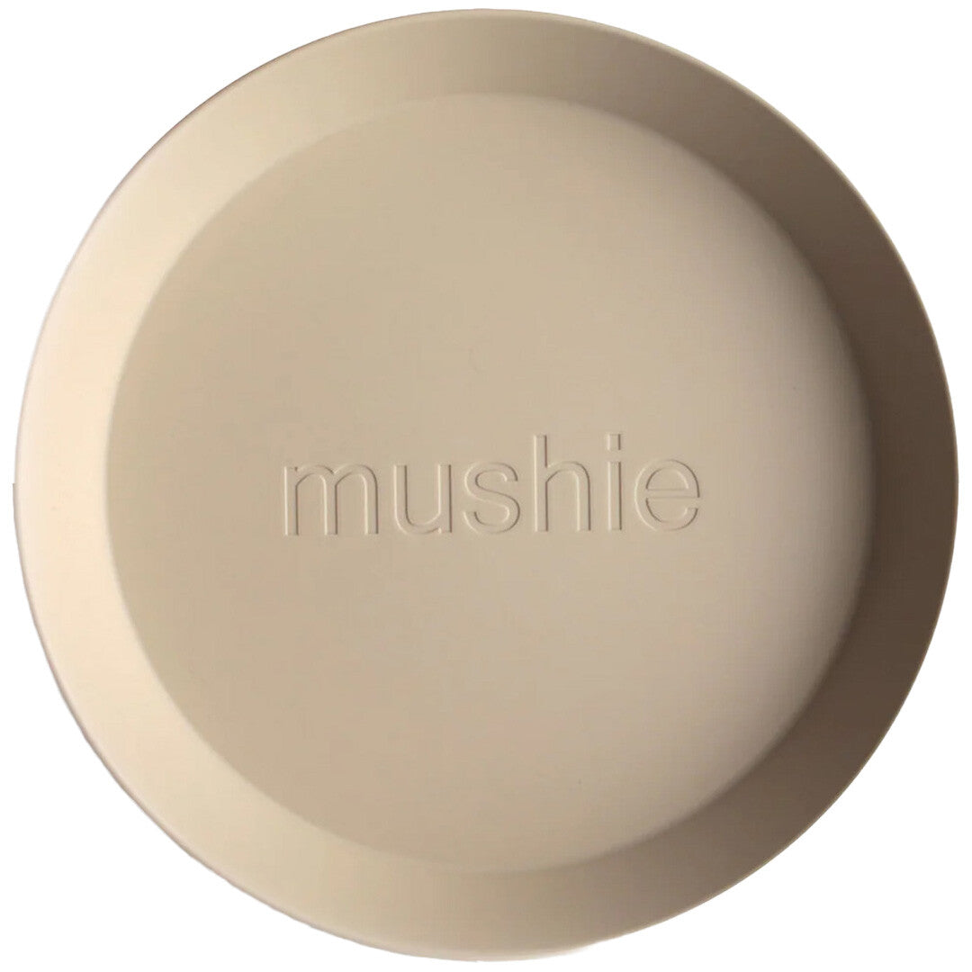 Een rond, beige mushie kinderbord met het logo in het midden, van bovenaf gezien.