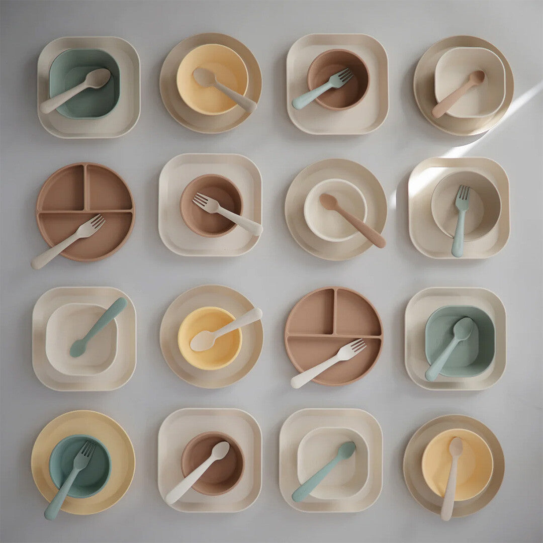Een collectie van zestien mushie kinderborden, kommen en besteksets in diverse pastelkleuren.