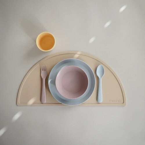 Een mushie kinderkom in zacht lila op een tafelsetting met bord, bestek en beker op een placemat.