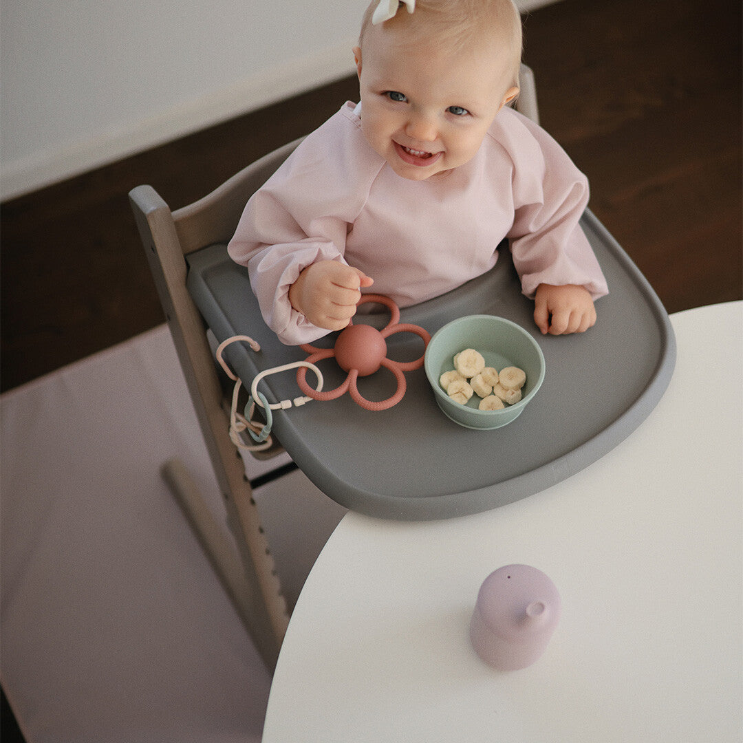 Lachende baby in een kinderstoel met een kommetje banaan op het eetblad.