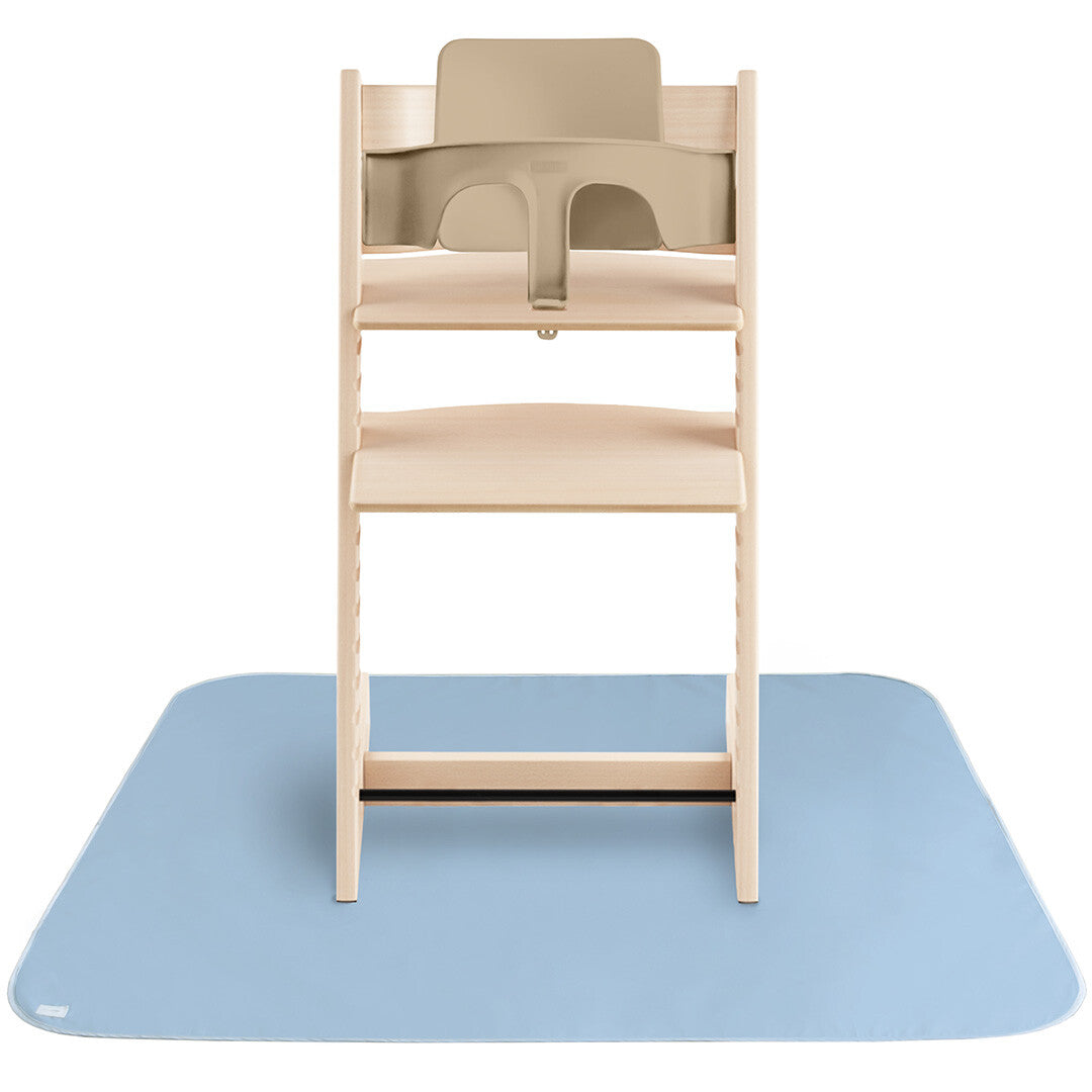 Een lichtblauwe mushie knoeimat ligt uitgespreid onder een houten kinderstoel met beige zitting.