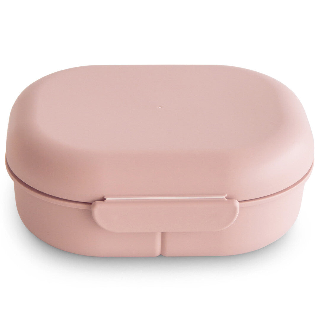 Mushie roze lunchbox met bestek, gesloten en schuin van bovenaf gefotografeerd.