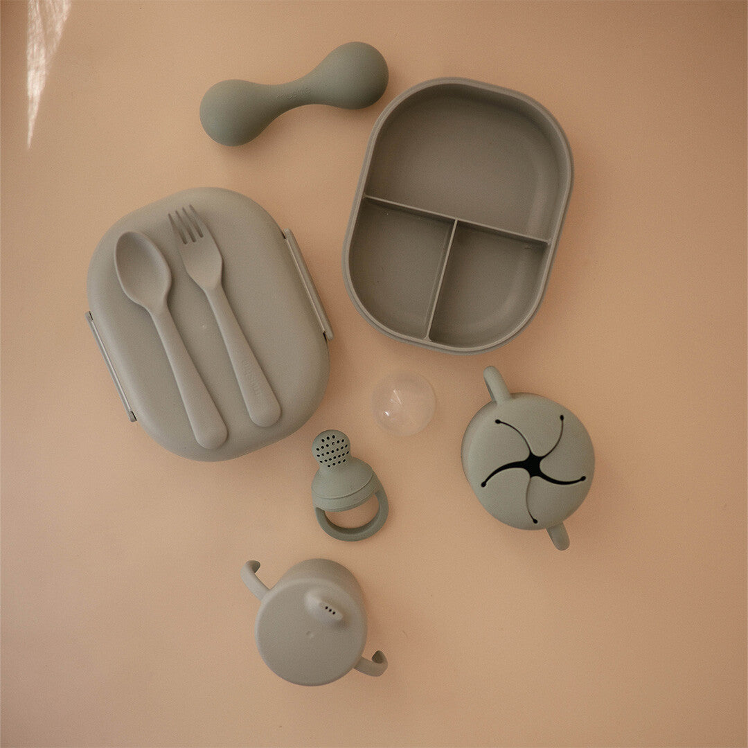 Collectie mushie baby- en kinderproducten in sage groen, waaronder een lunchbox en bestek.