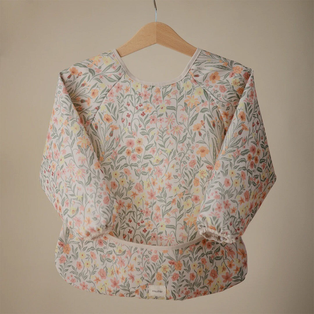 Mushie mouwslab voor baby's met een pastel bloemenpatroon, hangend aan een houten hanger.