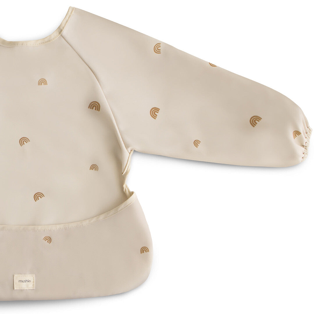 Detailopname van de Mushie beige mouwslab met regenboogpatroon en het merklabel.
