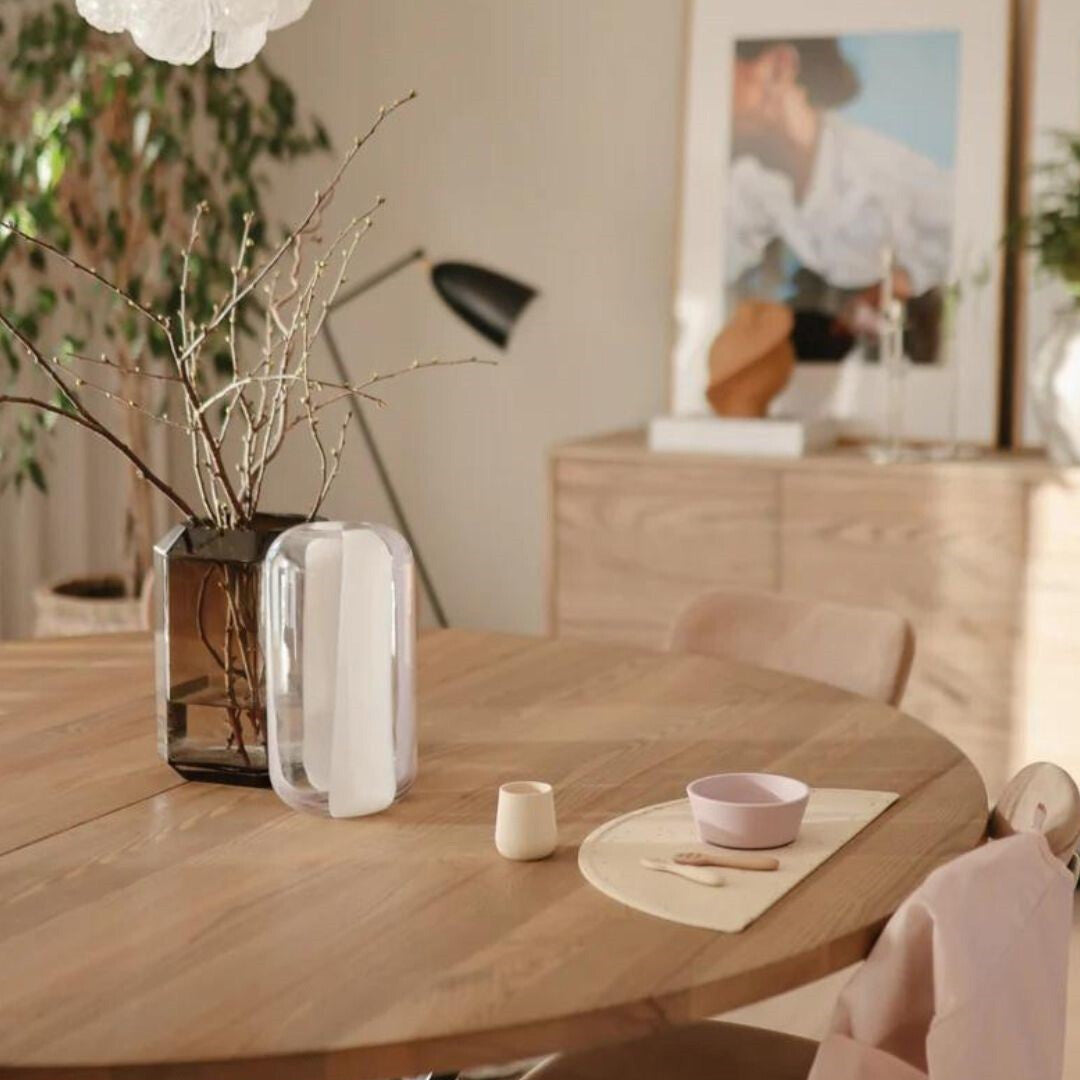 Een mushie peuterbeker in de kleur shifting sand en een roze kommetje op een houten tafel.