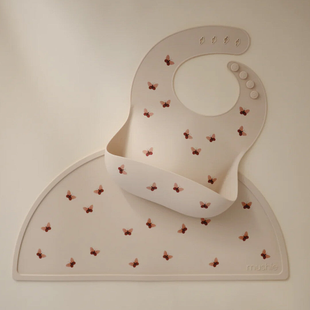 Mushie siliconen placemat en bijpassende slab in beige met vlinderpatroon.