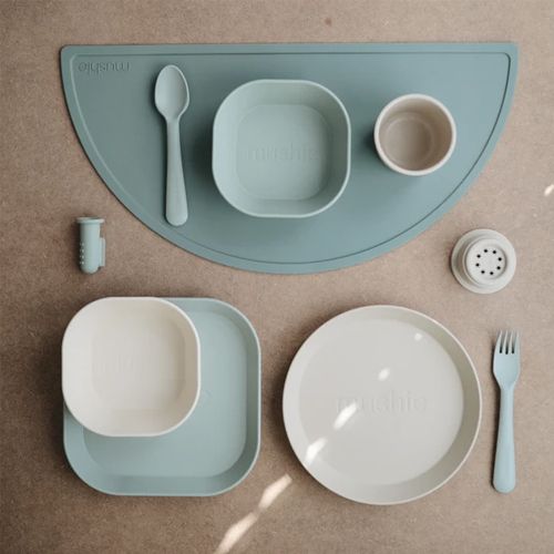 Mushie babyvoedingsset met borden, kommen, bestek en accessoires op een Cambridge blue placemat.