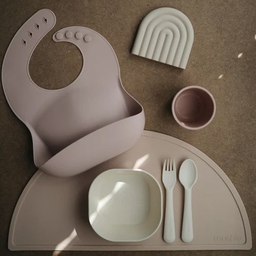 Mushie baby voedingsset met een roze slab, zandkleurige placemat, kom, beker en bestek.