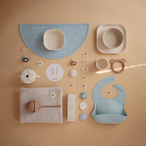 Collectie mushie babyvoedingsbenodigdheden en verzorgingsproducten, waaronder een blauwe placemat met stippen.