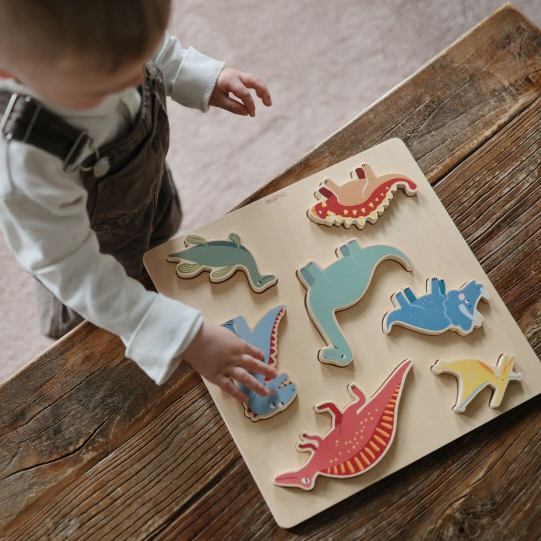 Een kind speelt met de Mushie houten dinosaurus puzzel op een rustieke houten tafel.