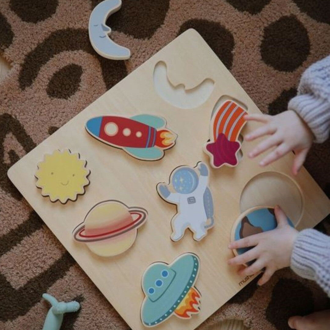Kinderhanden spelen met de mushie houten puzzel met ruimtefiguren.