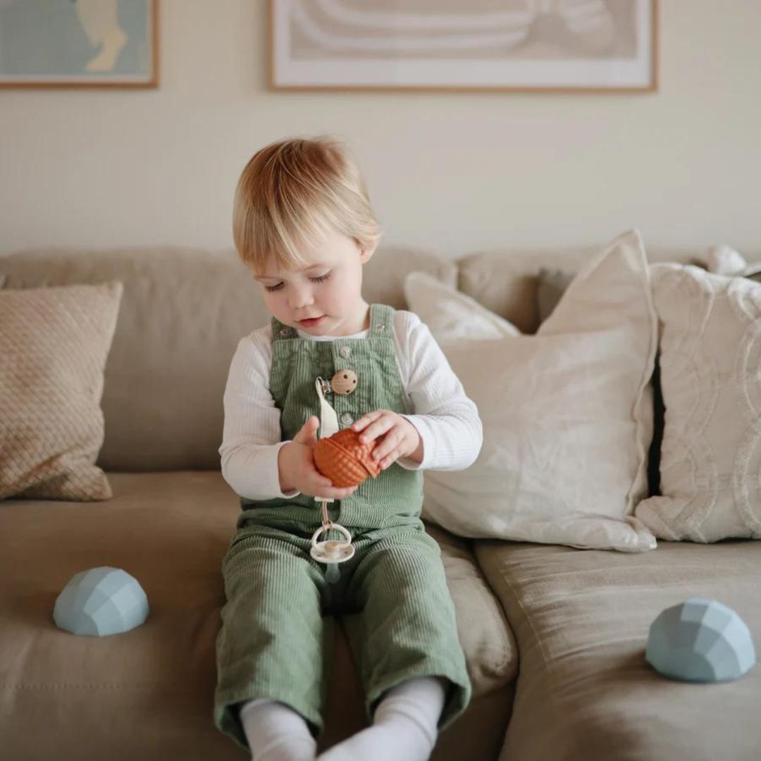 Een kind speelt op de bank met een oranje mushie sensorische bal, met twee lichtblauwe ballen ernaast.