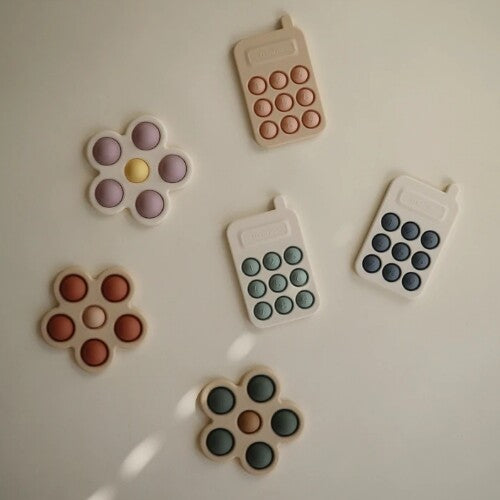 Een collectie van mushie sensorische bloem en telefoon babyspeelgoed in diverse kleuren.