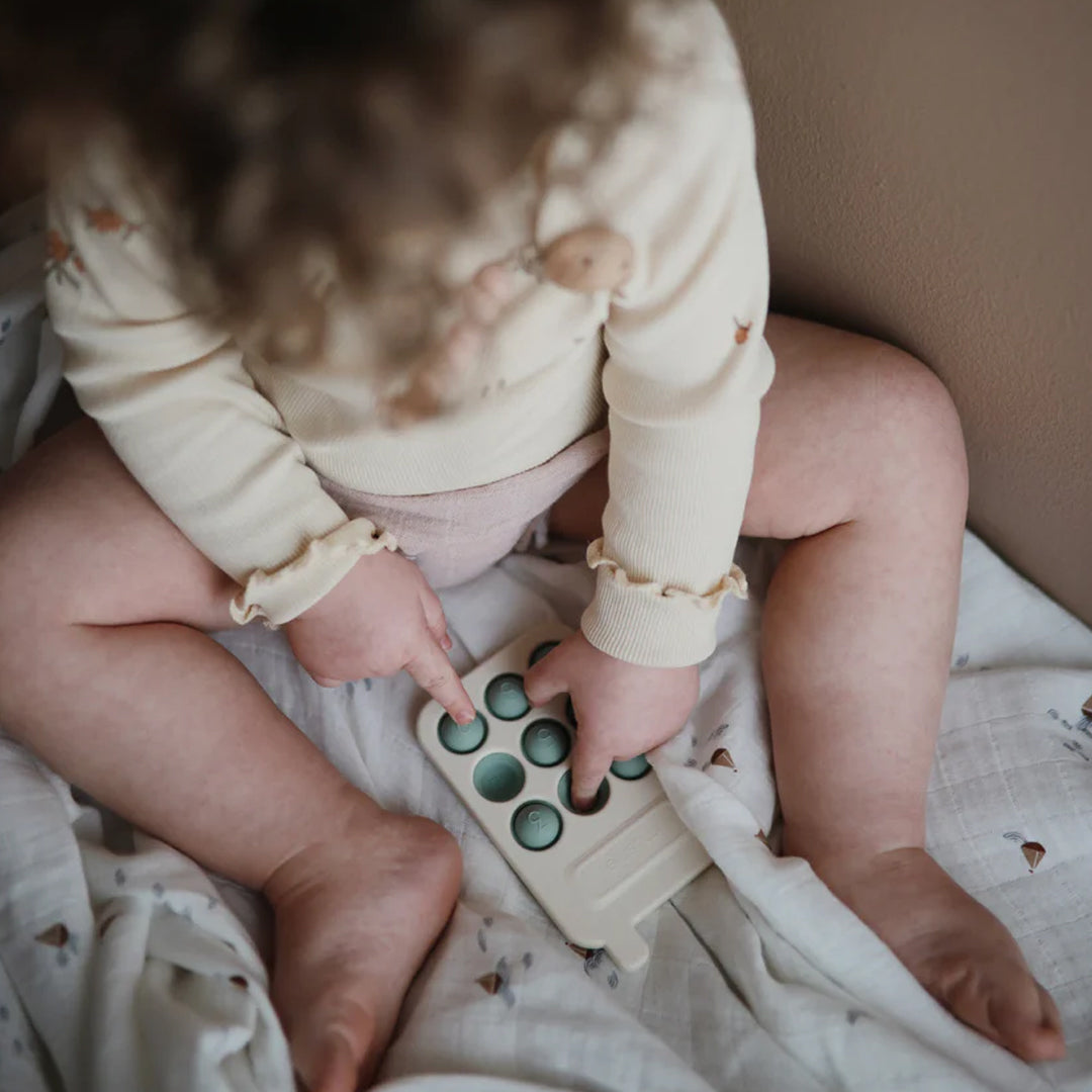 Een baby speelt met een beige sensorische speelgoedtelefoon.