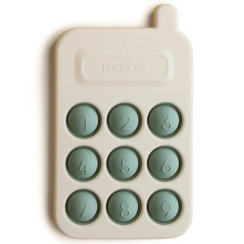 Mushie sensorische speelgoedtelefoon in beige met groene genummerde knoppen.